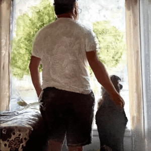 Portrait of a man reflecting on the scene outside a window with his dog